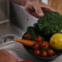 A close-up of fresh vegetables including broccoli, lemon, and tomatoes in a kitchen.