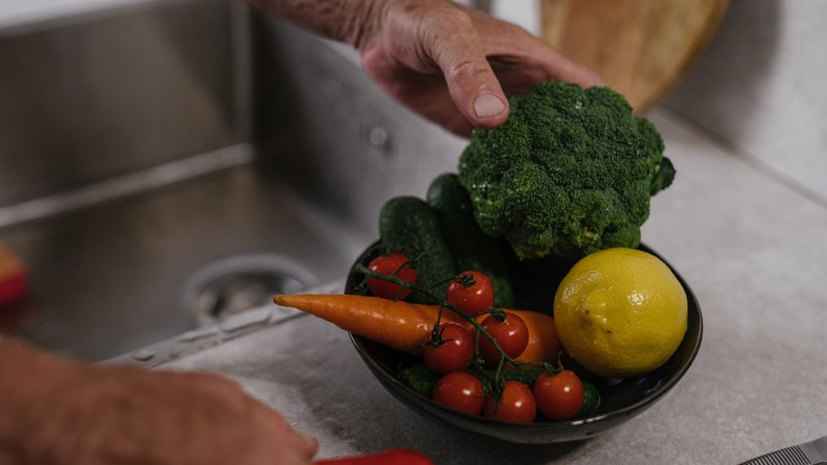 A close-up of fresh vegetables including broccoli, lemon, and tomatoes in a kitchen.