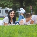 Happy family lying on grass with RV in the background, enjoying a sunny outdoor picnic.