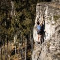 A woman ascending a rock face surrounded by a lush forest in Trutnov, Czechia.